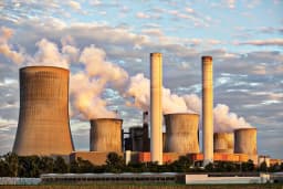 Coal-fired power plant with cooling towers emitting steam plumes against a dramatic sunset sky, illustrating the industrial emissions at the center of the EPA endangerment finding dispute