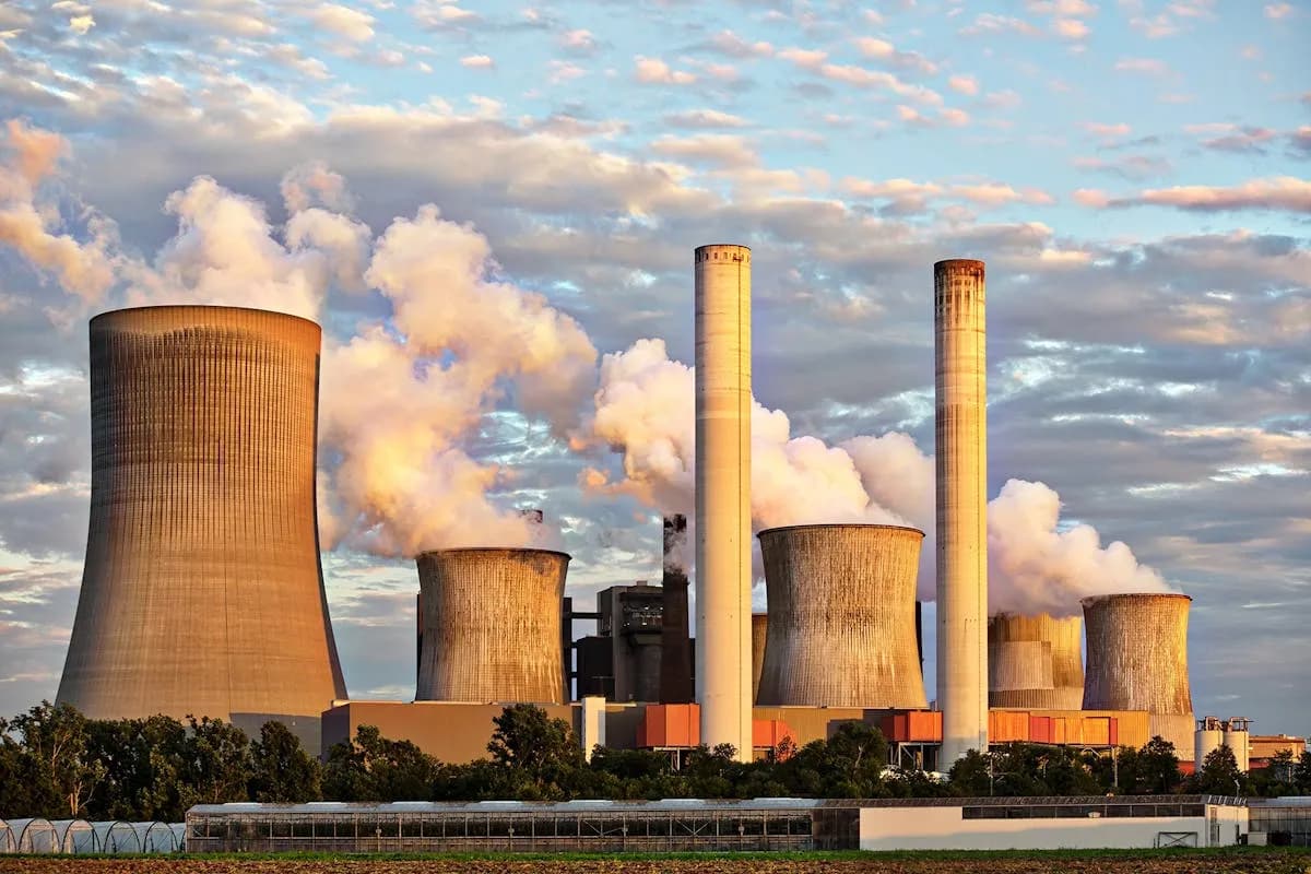 Coal-fired power plant with cooling towers emitting steam plumes against a dramatic sunset sky, illustrating the industrial emissions at the center of the EPA endangerment finding dispute