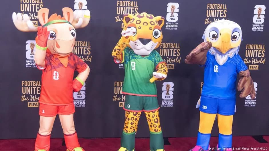 Three 2026 World Cup mascots pose in front of a FIFA 'Football Unites the World' backdrop.