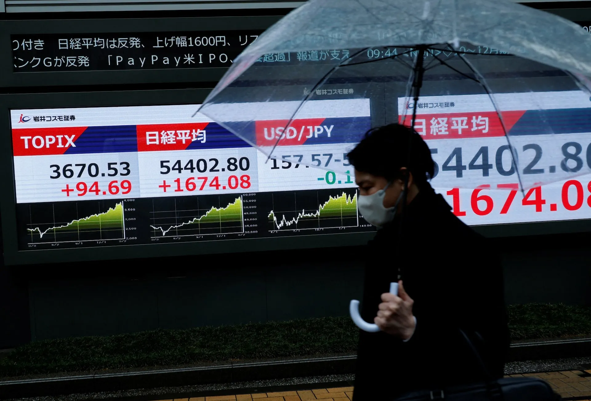 A pedestrian walks past a stock quotation board showing the Topix and Nikkei averages in Tokyo as oil prices surge amid the Iran war