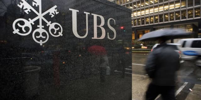 A pedestrian walks past the UBS headquarters on Park Avenue in New York City, with the UBS logo prominently displayed on the building facade