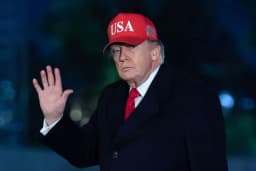 A man waves outdoors in a dark suit and red tie.