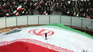 A boy raises his fist while standing on a giant Iranian flag during the funeral of IRGC navy commander Alireza Tangsiri in Tehran on April 1, 2026