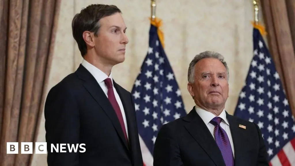 Jared Kushner and Steve Witkoff stand indoors in dark suits with U.S. flags behind them.