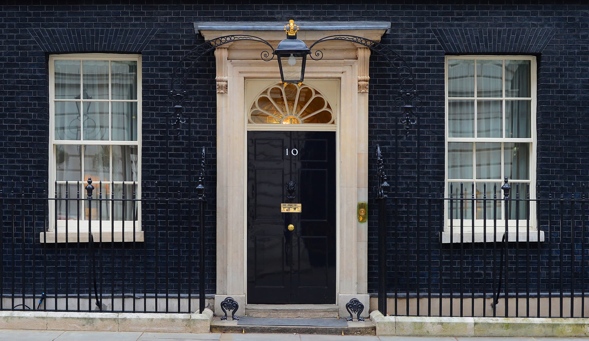 The black front door of 10 Downing Street with its characteristic white frame and brass number plate, seen from the street in London