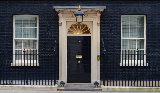 The black front door of 10 Downing Street with its characteristic white frame and brass number plate, seen from the street in London