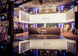 The Munich Security Conference stage with conference branding and camera equipment in a large hotel ballroom