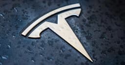 A close-up of a Tesla logo on a wet vehicle surface
