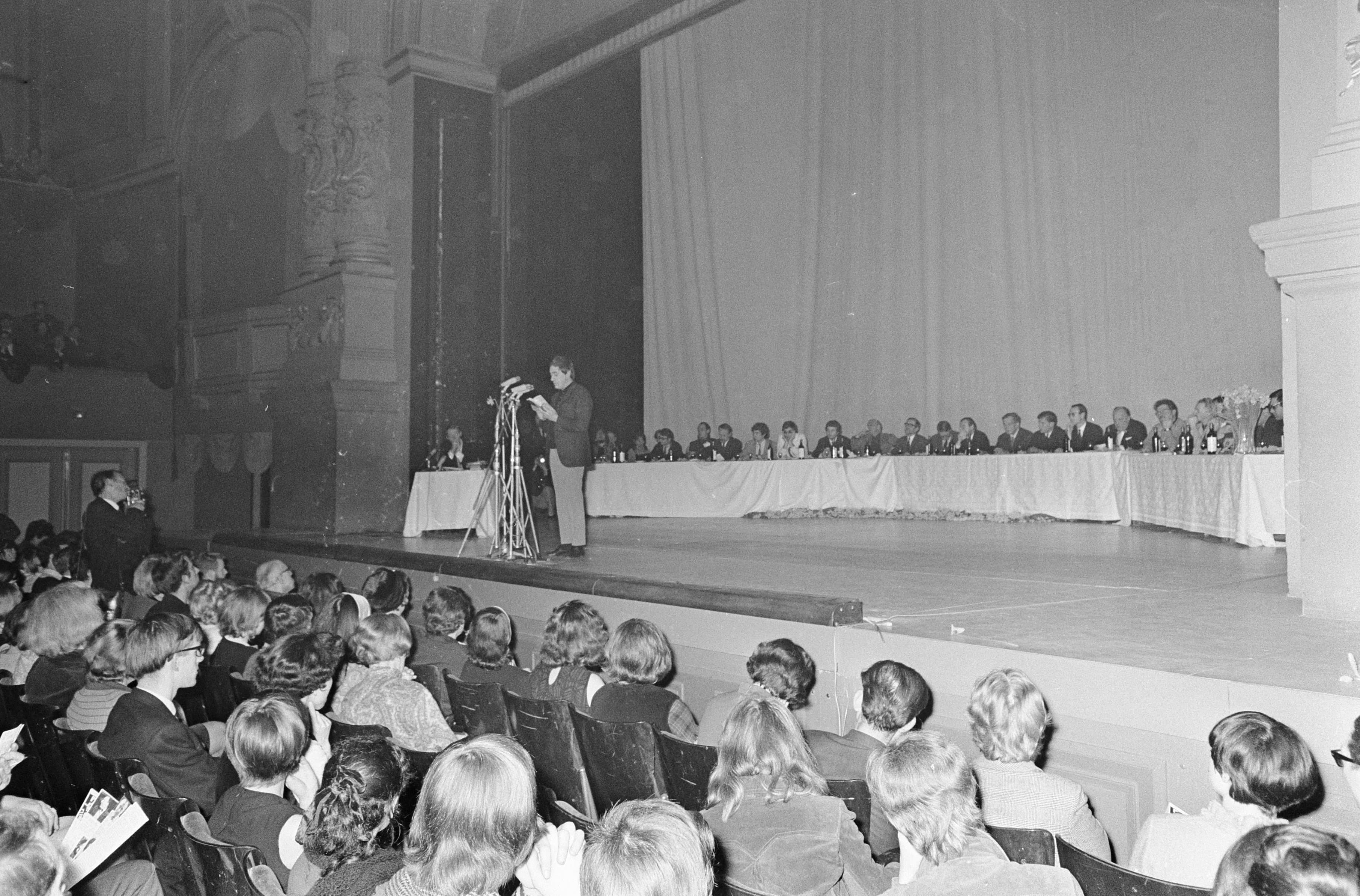 A writer delivering a reading at a literary event in a grand theatre setting